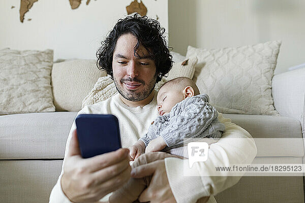 Father using smart phone with baby boy sleeping at home