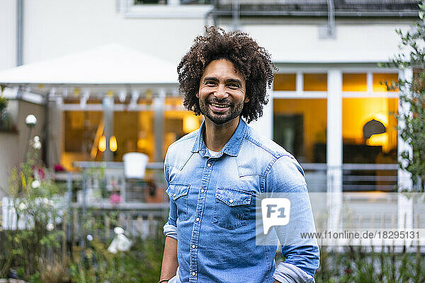 Happy man with afro hairstyle standing in front of house