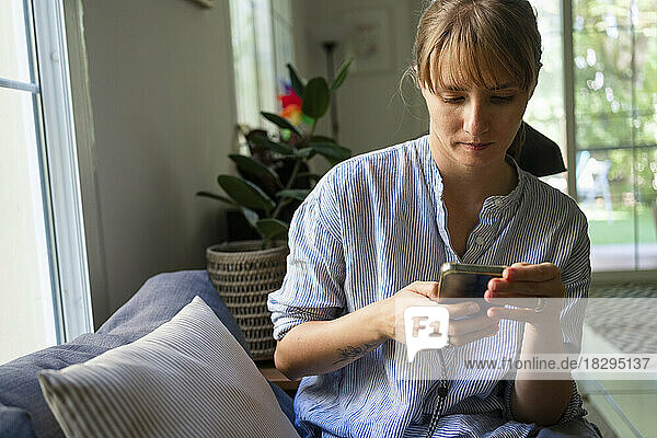 Woman using smart phone on sofa at home