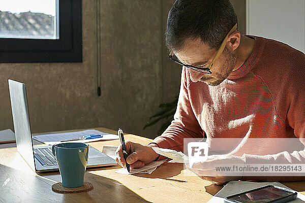 Man writing with pen and examining financial bills at home