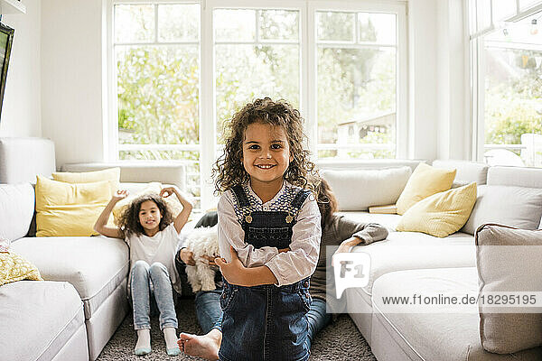 Glückliches Mädchen steht im Wohnzimmer mit der Familie im Hintergrund zu Hause