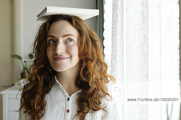 Smiling woman balancing book on head at home