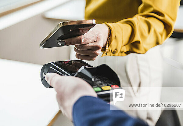 Young woman paying with smart phone on card reader machine