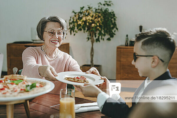 Glückliche Großmutter  die ihrem Enkel im Café ein Stück Pizza gibt