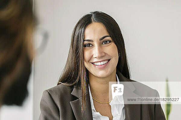Smiling businesswoman looking at colleague in front of white wall