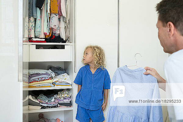 Father holding dress looking at daughter leaning on closet