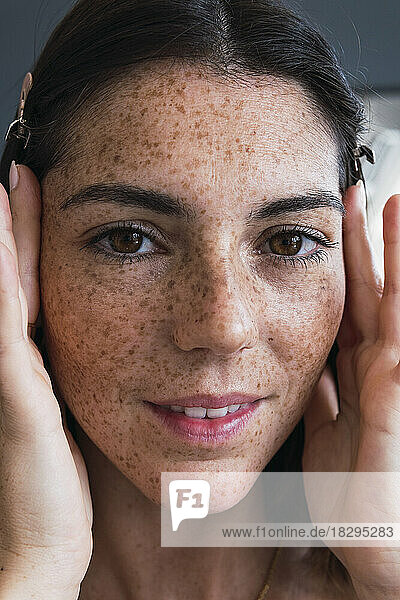 Smiling woman with freckle face applying moisturizer on face at home