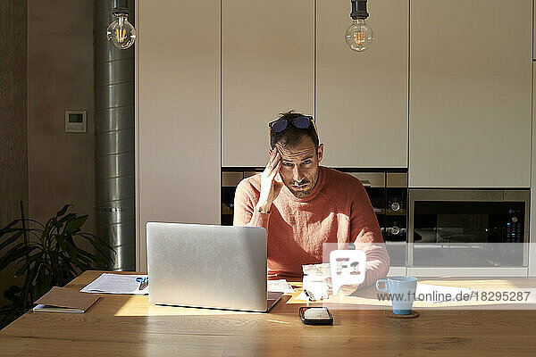 Gestresster Mann sitzt zu Hause mit Finanzrechnungen auf dem Schreibtisch