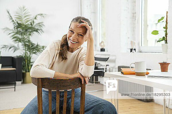 Happy mature businesswoman with head in hand sitting on chair at office