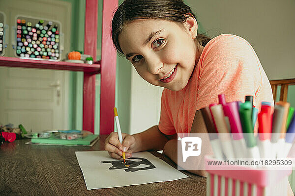 Smiling girl coloring cat picture on paper at home