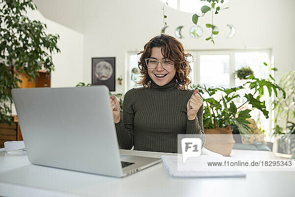 Excited freelancer sitting in front of laptop at home