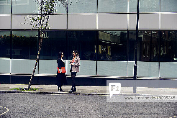 Young businesswoman talking with colleague standing at footpath