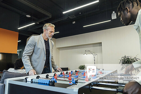 Mature businessman playing foosball with young colleague in office