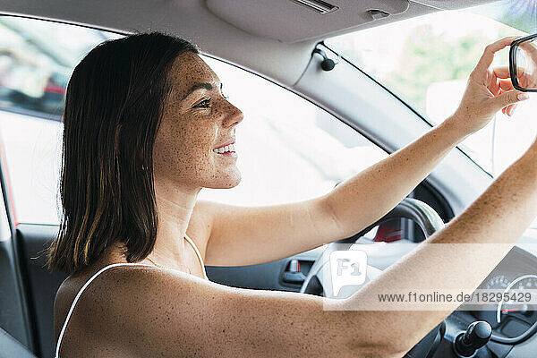 Glückliche Frau arrangiert Rückspiegel im Auto