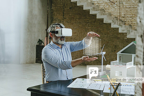 Geschäftsmann mit VR-Brille gestikuliert mit Musterhaus auf Schreibtisch auf Baustelle