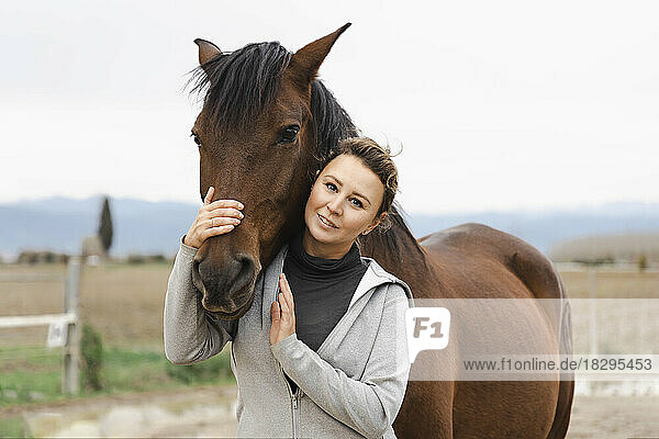 Lächelnde Frau umarmt braunes Pferd auf der Ranch