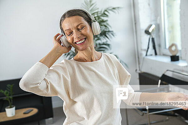 Happy businesswoman wearing headphones listening music and dancing in office