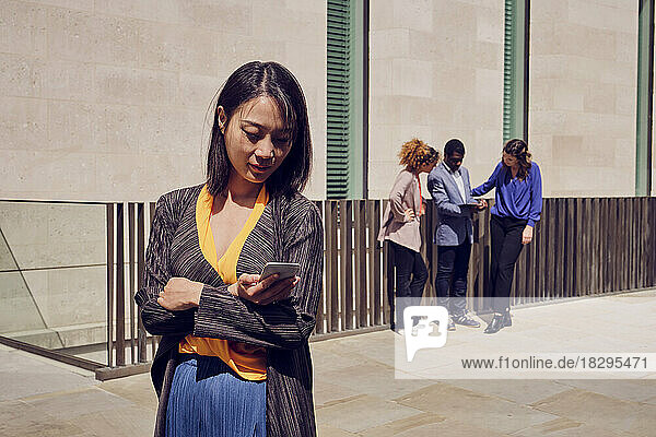 Businesswoman using smart phone with colleagues standing in background