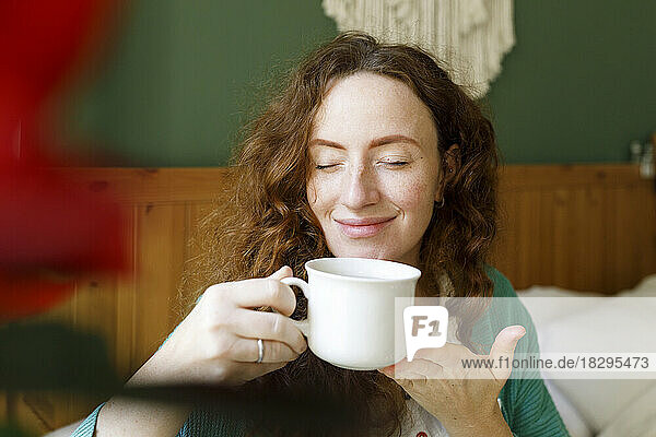 Lächelnde Frau mit geschlossenen Augen  die zu Hause Tee trinkt