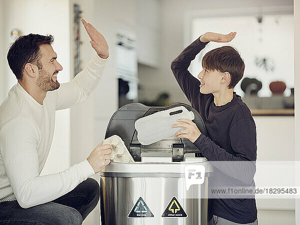 Father and son sorting waste paper and plastic into a sorting bin
