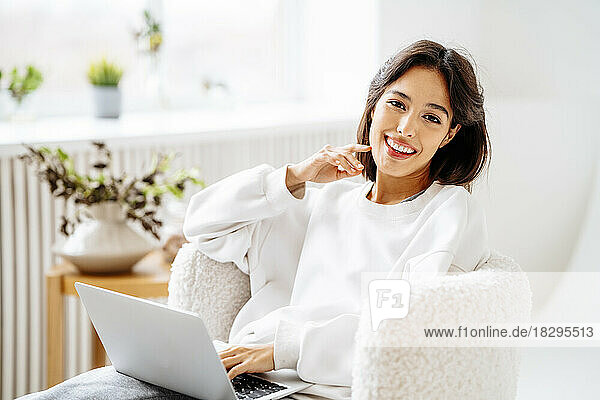 Happy young woman with laptop sitting on chair