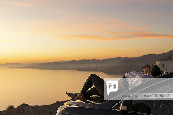 Woman relaxing on hood of car at sunset