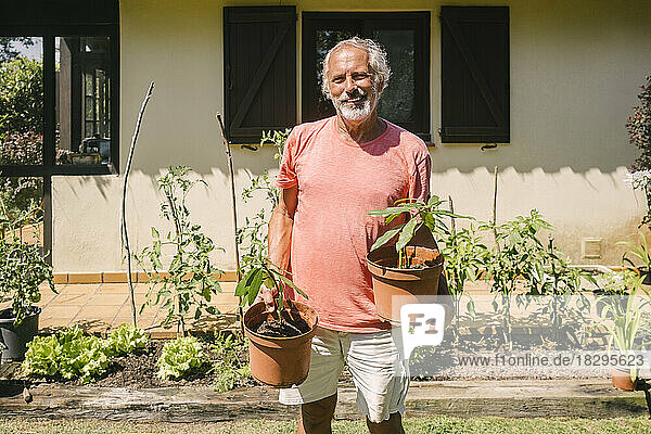 Happy senior man holding potted plant outside house