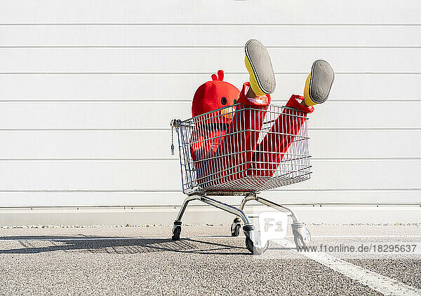 Woman wearing red duck costume sitting in shopping cart in front of wall