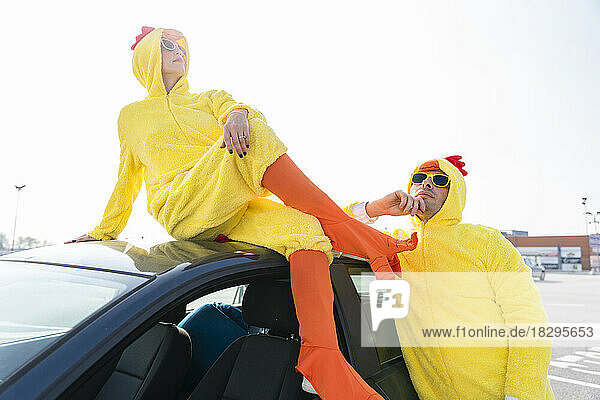 Woman in yellow chicken costume sitting on car with thoughtful man in parking lot