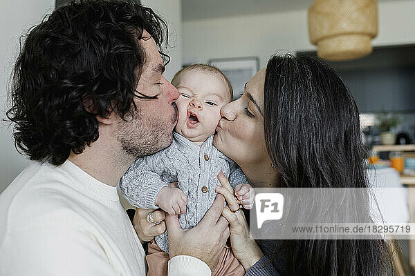 Father and mother kissing baby boy at home