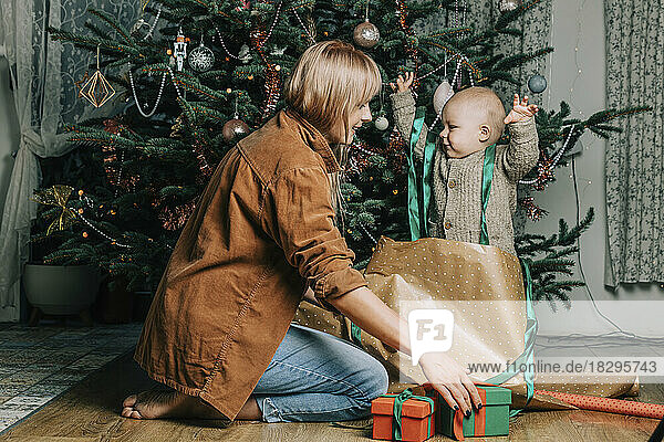 Happy mother with son playing by Christmas tree at home