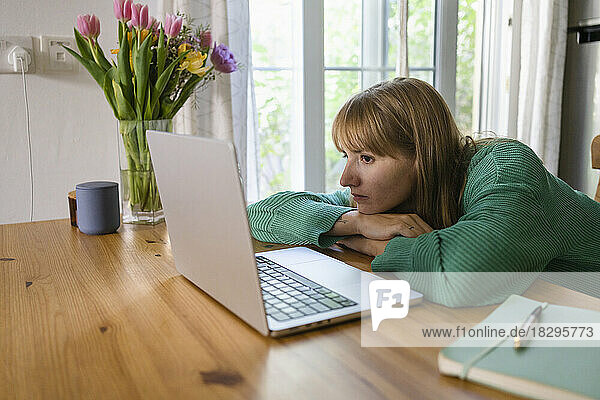 Freelancer with laptop leaning on table at home
