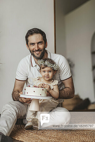 Smiling father and daughter holding birthday cake at home