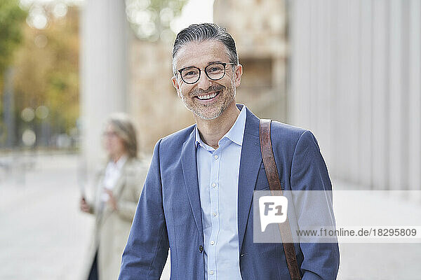 Happy mature businessman in blazer standing on footpath