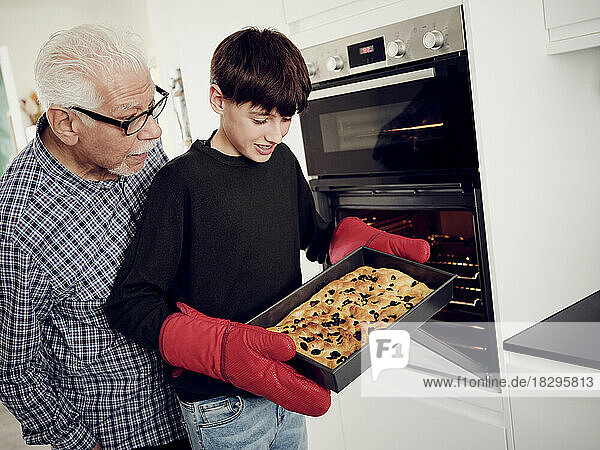 Grandfather and grandson holding baking tray with fresh focaccia bread in the kitchen