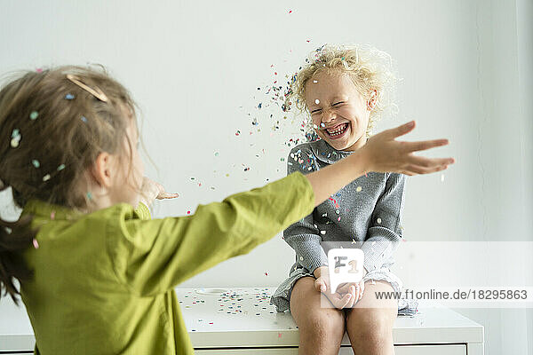 Happy girl throwing confetti on friend at home