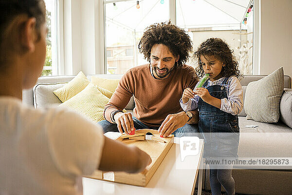 Smiling father playing board games with daughters at home