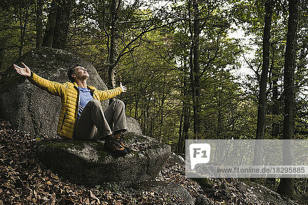 Carefree mature man with arms outstretched sitting on rock