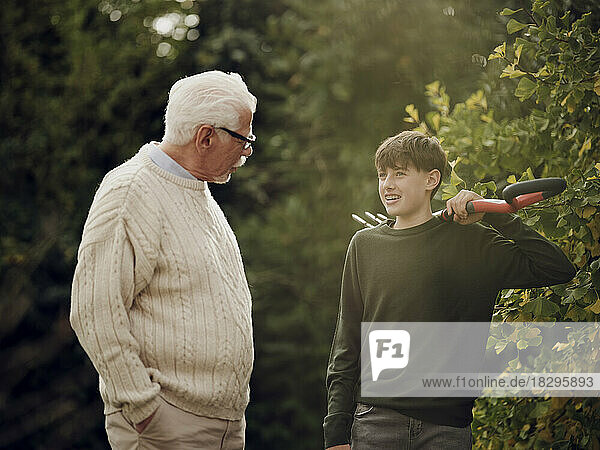 Grandfather and grandson talking in garden boy carrying garden fork