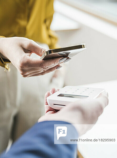 Hand einer jungen Geschäftsfrau  die per Smartphone und Kreditkartenleser bezahlt