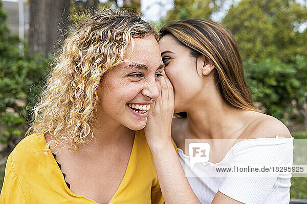 Young woman whispering into friend's ear in park