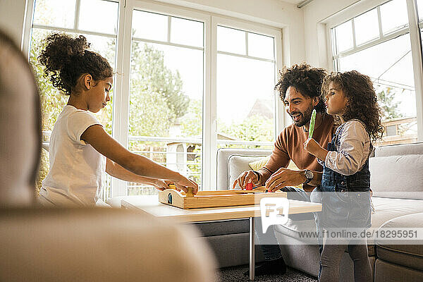 Happy father playing board games with daughters at home