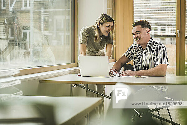 Smiling businesswoman and businessman discussing over laptop in office