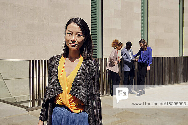 Smiling businesswoman with colleagues standing in background on sunny day