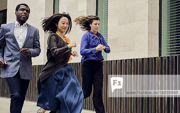 Businessman and businesswoman with colleague checking time running together on footpath