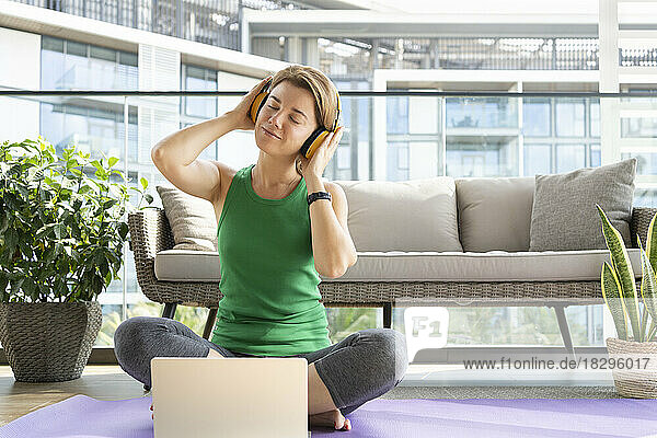 Smiling woman wearing headphones listening to music sitting on balcony