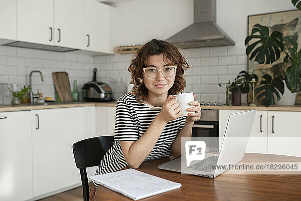 Freelancer with cup of coffee sitting with laptop at table