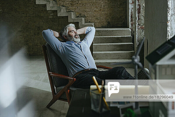 Thoughtful architect resting in chair with hands behind head at under construction site