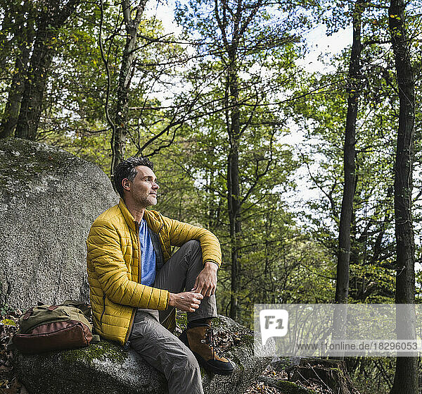 Man with backpack sitting on rock in forest