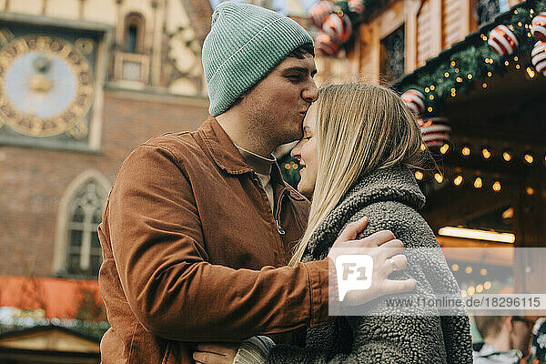 Mann küsst Frau auf dem Weihnachtsmarkt auf die Stirn
